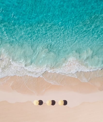 An aerial view of three yellow beach umbrellas in sand by the water.